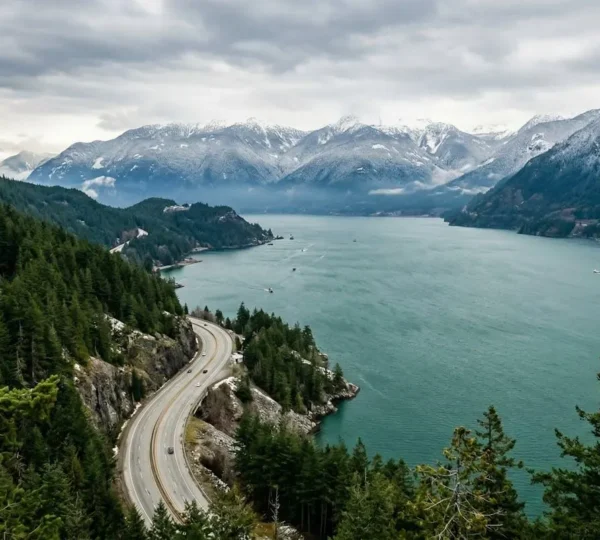 Scenic coastal highway winding along turquoise ocean fjord with dramatic mountain peaks and evergreen forest in British Columbia